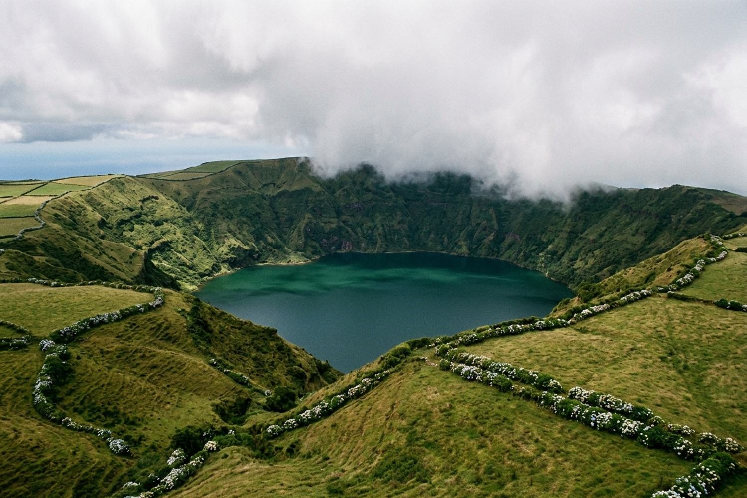 A deep green crater lake ringed by very steep grassy slopes under broken cloud.