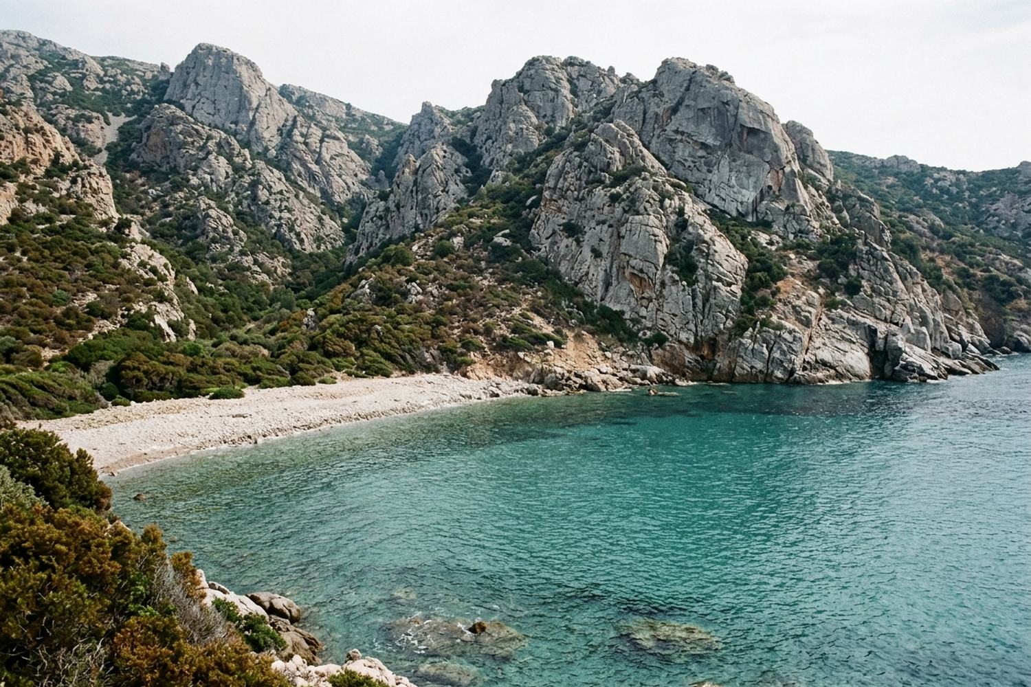 Grey granite mountains dropping into a small cove of clear turquoise water.